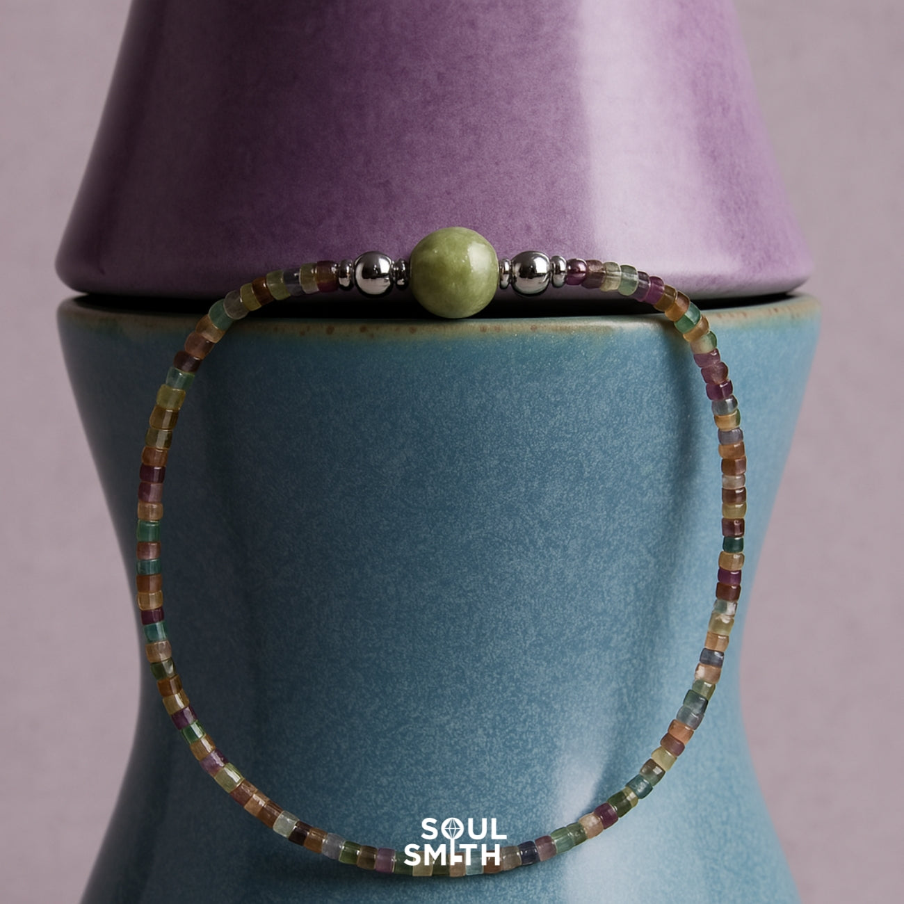 Minimalist bracelet with a Berylite center bead and multicolored square-cut gemstone strand, styled on stacked ceramic vases.