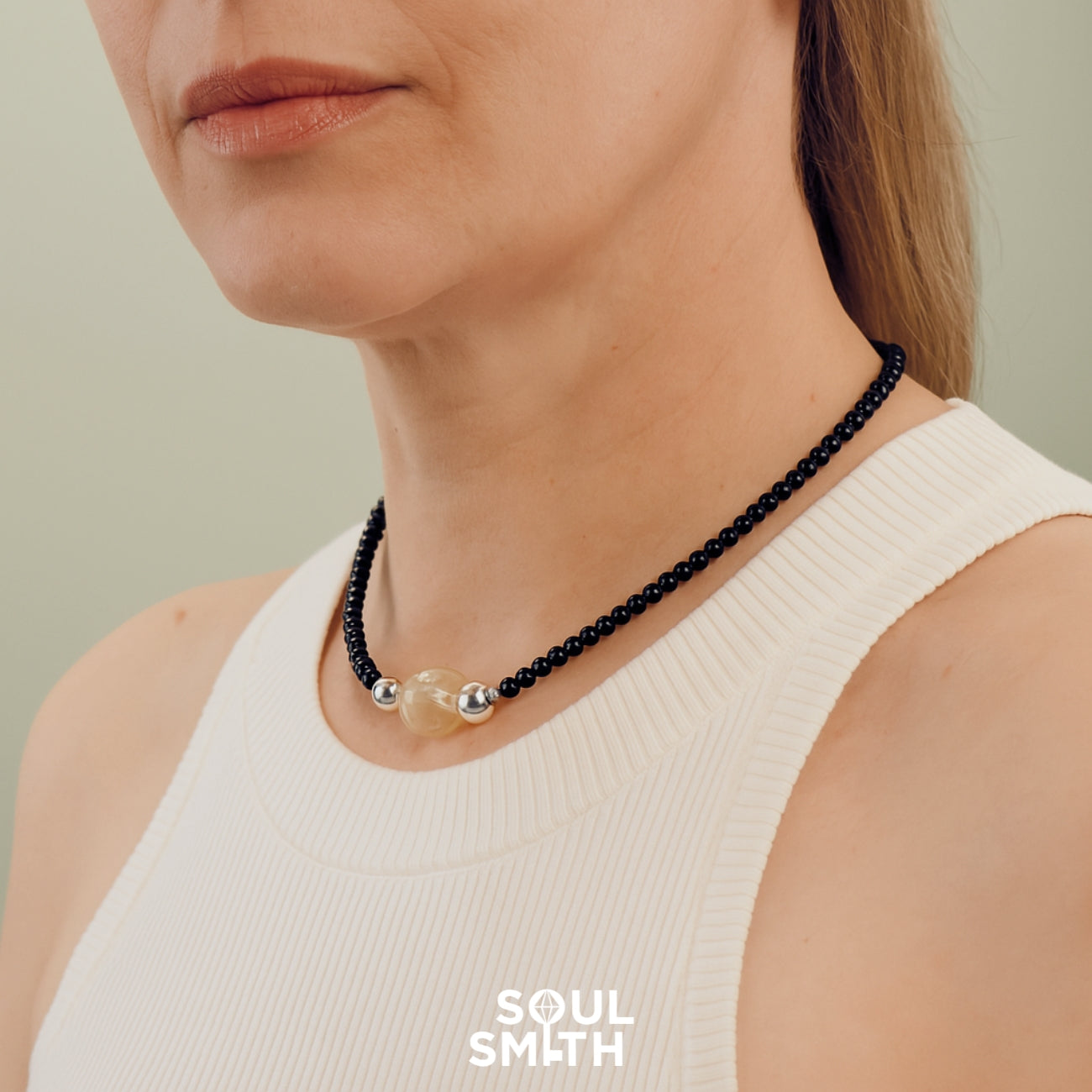 Close-up of a woman wearing a SoulSmith necklace with black beads and a central golded rutilated quartz charm, symbolizing clarity and spiritual strength.