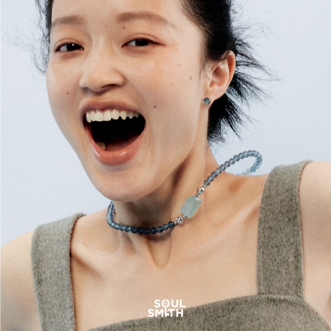 Smiling woman wearing a Soulsmith Aquamarine crystal necklace with hexagonal pendant and blue round beads – joyful expression highlights the calming and expressive energy of Aquamarine.