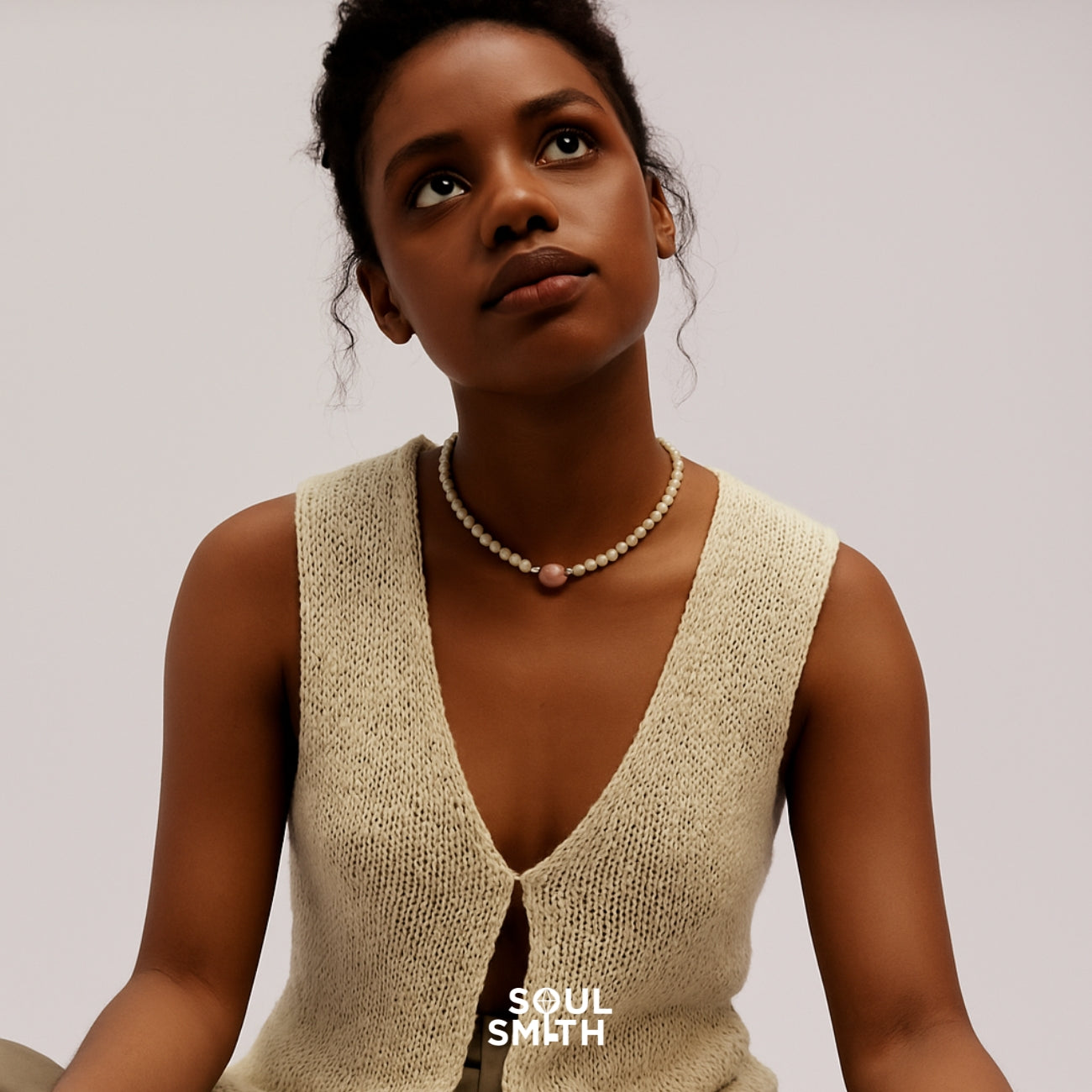 Woman wearing a delicate Soulsmith necklace featuring a central Pink Morganite charm and creamy ivory beads, styled with a natural knit sleeveless top, evoking softness and serenity.
