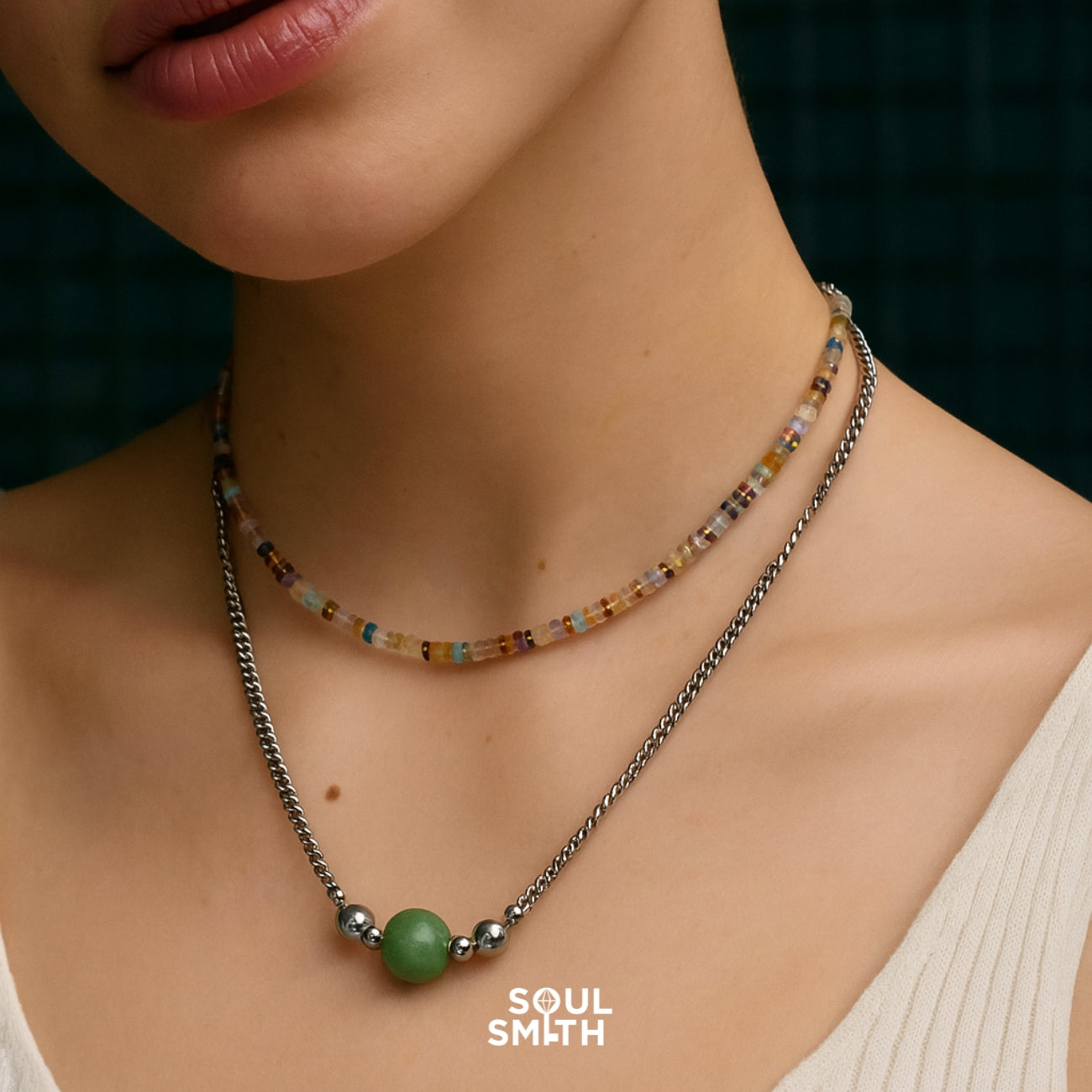 Layered necklace set featuring a multicolored square-cut beaded choker paired with a twisted silver chain and a central green Berylite charm, styled against a cream-toned top.