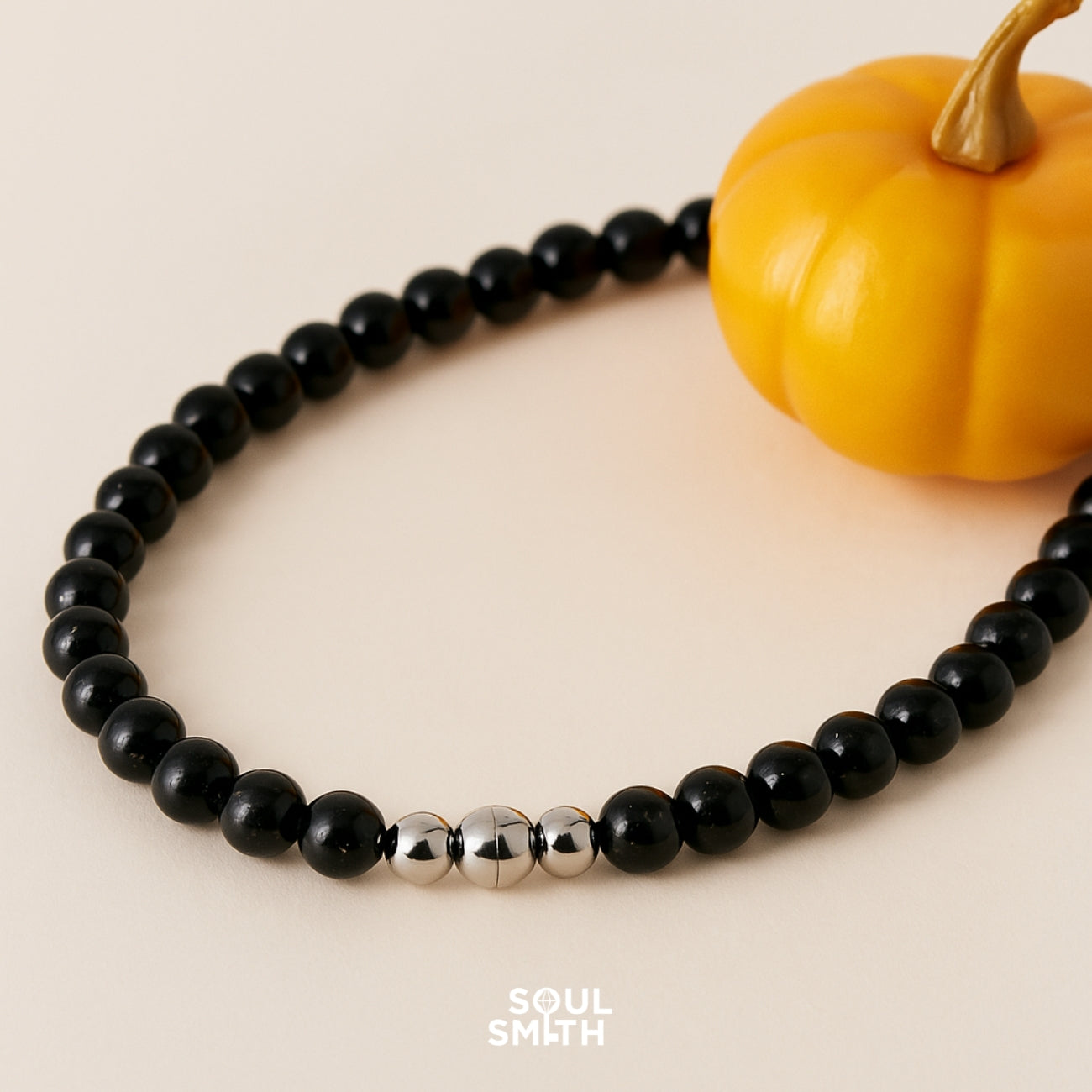Close-up of Soulsmith black onyx bead necklace with polished silver clasp, styled beside a mini pumpkin for an autumn-inspired grounding and protection aesthetic.