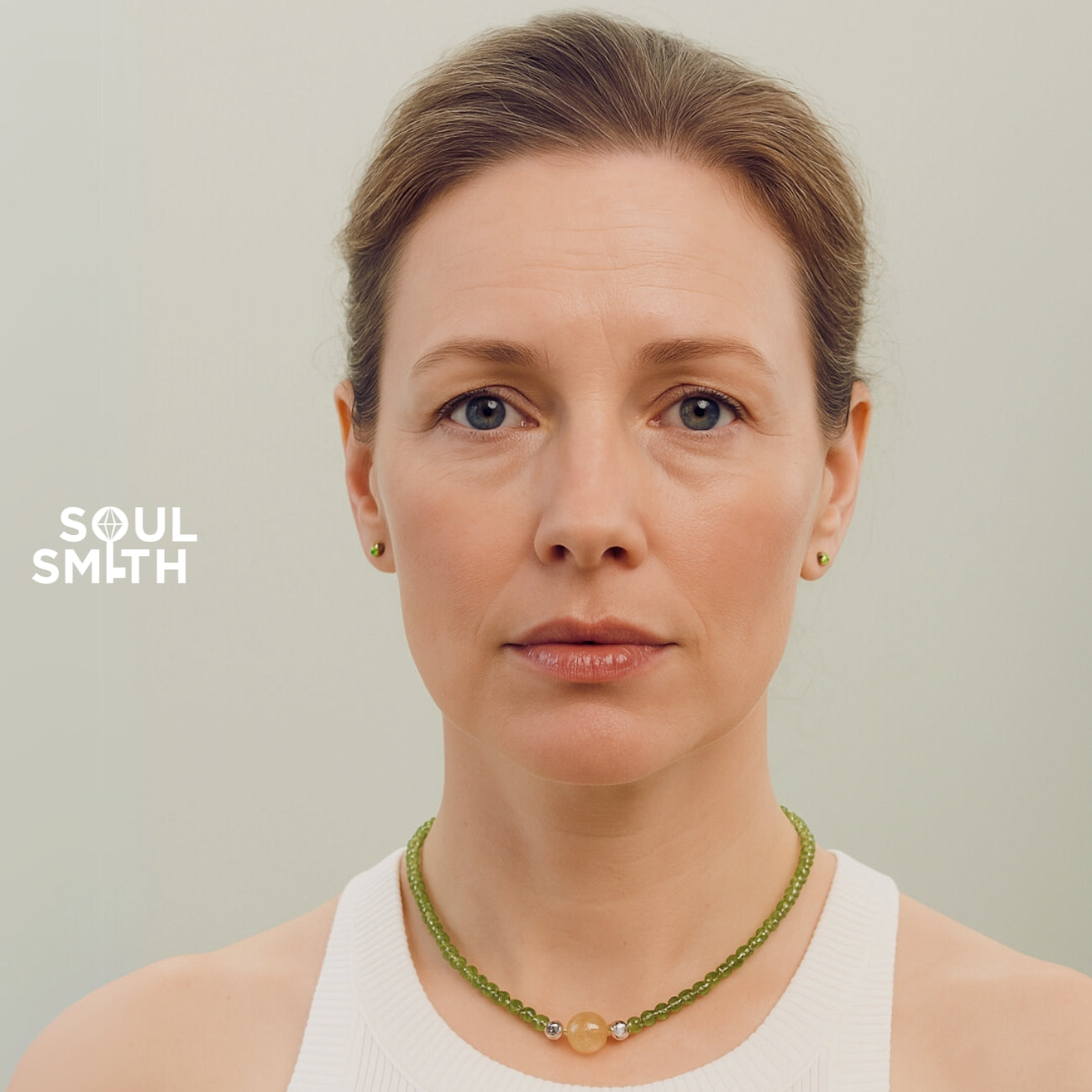 Woman wearing a SoulSmith necklace featuring a golden rutilated quartz charm paired with green peridot beads, radiating warmth and personal empowerment.