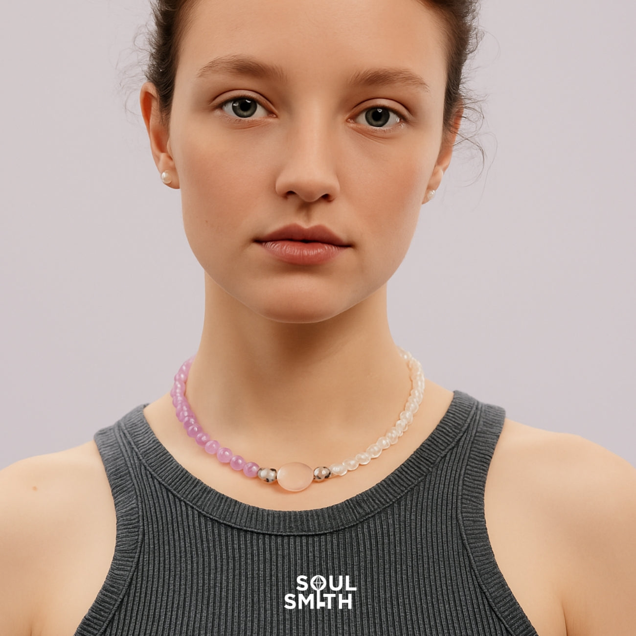 Woman wearing a SoulSmith crystal necklace handcrafted with a blend of lavender amethyst and clear quartz beads, centered with a polished rose quartz focal stone—chakra-aligned healing jewelry on a minimalist backdrop.