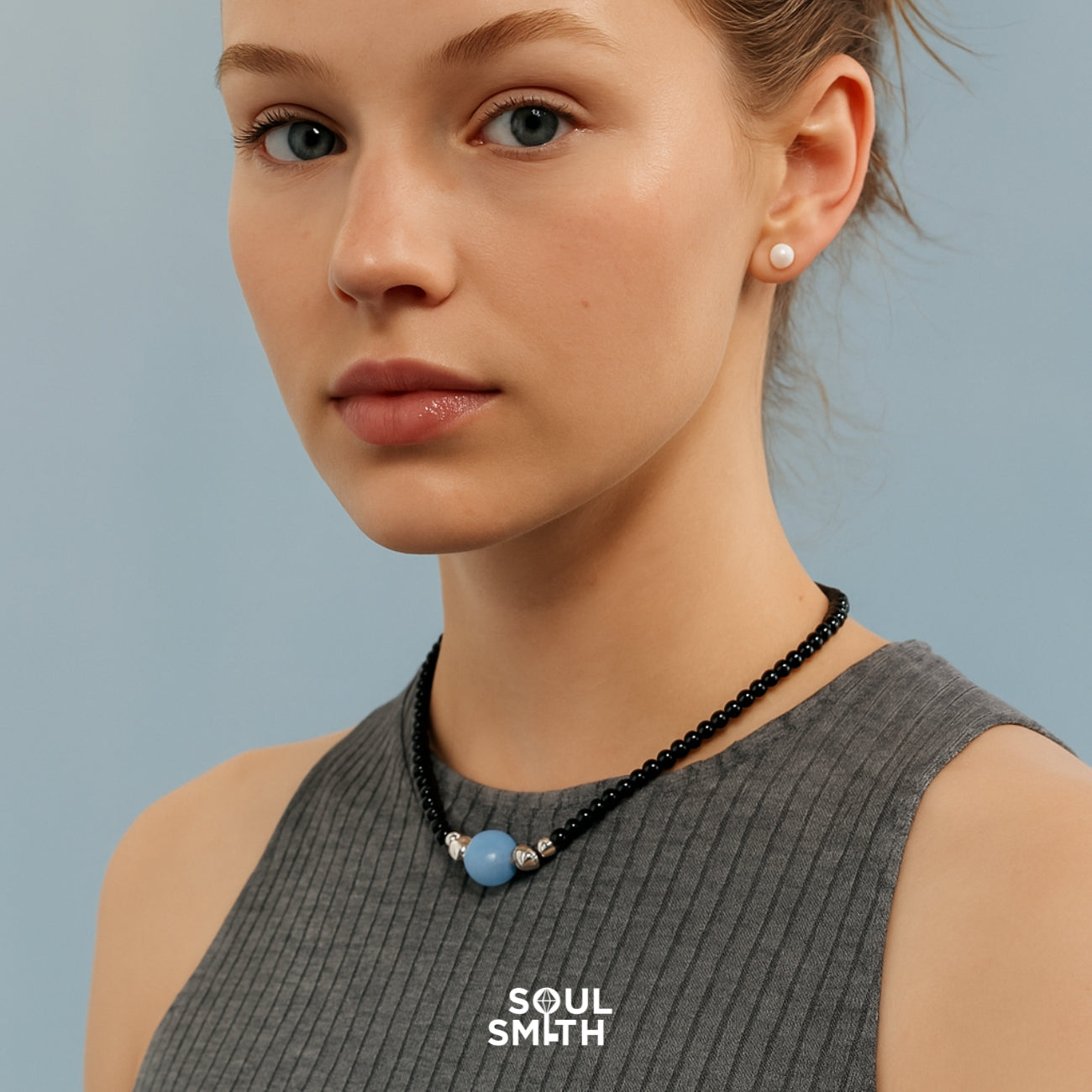 Woman wearing Soulsmith black onyx necklace with round blue lace agate centerpiece and silver accents, designed for grounding, communication, and throat chakra healing.
