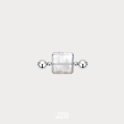 Square-cut Blue Needle Crystal charm flanked by polished silver beads, showcasing delicate thread-like inclusions in a translucent, icy base — an ethereal element from the Soulsmith SoulLinks collection.
