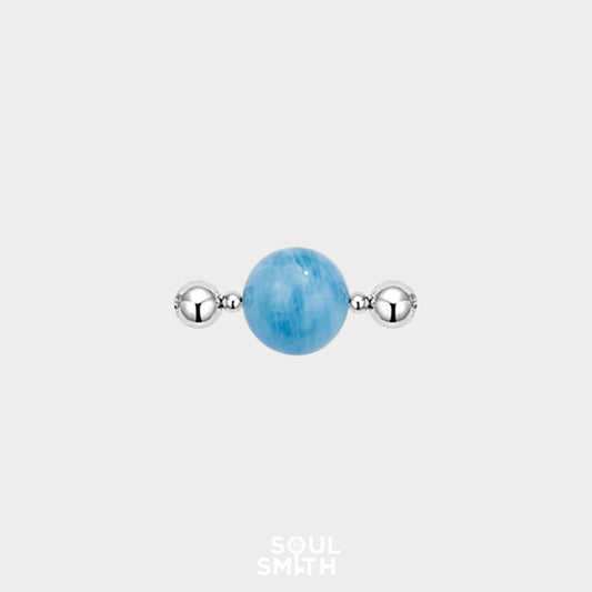 Soulsmith charm featuring a polished aquamarine gemstone centered between two reflective silver beads, set against a light grey background.


