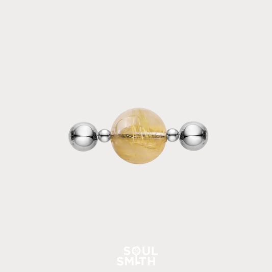 Round Golden Rutilated Quartz charm featuring golden needle-like inclusions, set between two polished silver spacer beads on a light background.
