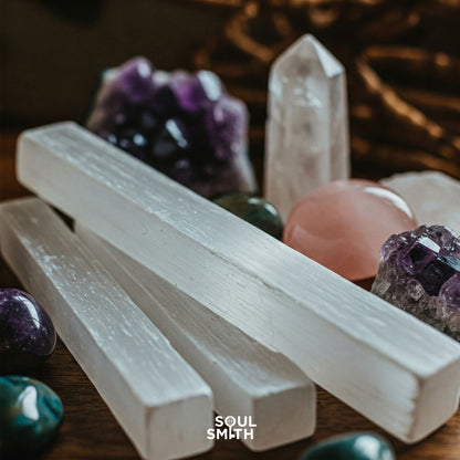 White selenite sticks displayed with polished chakra crystals, including rose quartz, amethyst, and clear quartz points. A grounding and cleansing crystal arrangement by Soulsmith.
