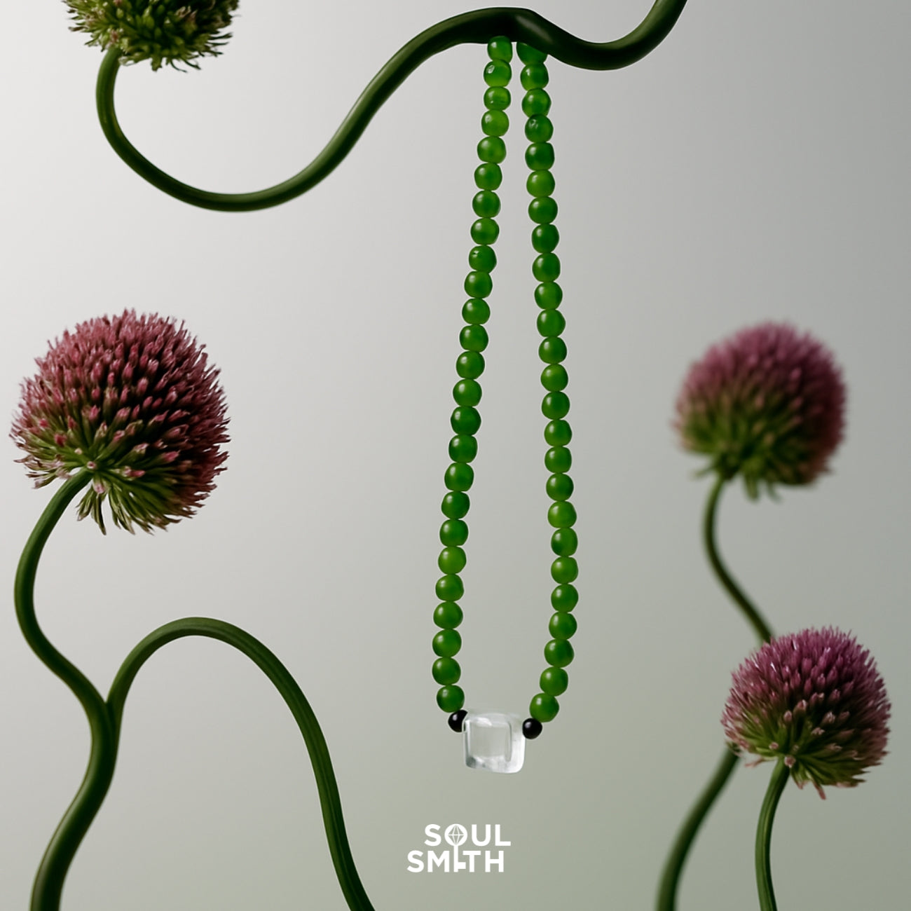 Jade beaded necklace with a square-cut blue needle clear quartz centerpiece and black accent beads, artfully suspended among sculptural allium flowers — a statement piece from the Soulsmith SoulLinks collection.
