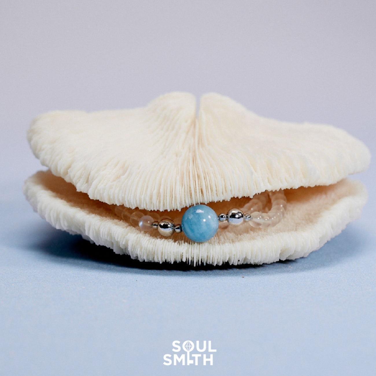 Aquamarine gemstone bracelet with silver accents, elegantly displayed in an open ivory coral shell, evoking oceanic calm and coastal elegance.

