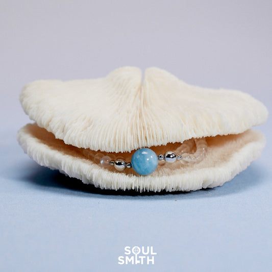 Aquamarine gemstone bracelet with silver accents, elegantly displayed in an open ivory coral shell, evoking oceanic calm and coastal elegance.


