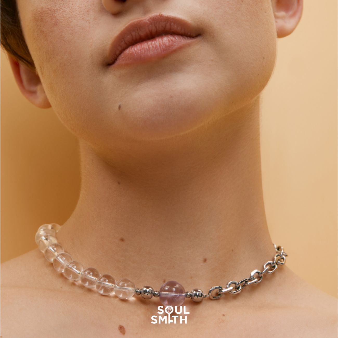 Close-up of a woman wearing a mixed-media choker featuring clear quartz crystal beads and a single amethyst centerpiece, paired with a bold silver chain and magnetic clasp from Soulsmith.
