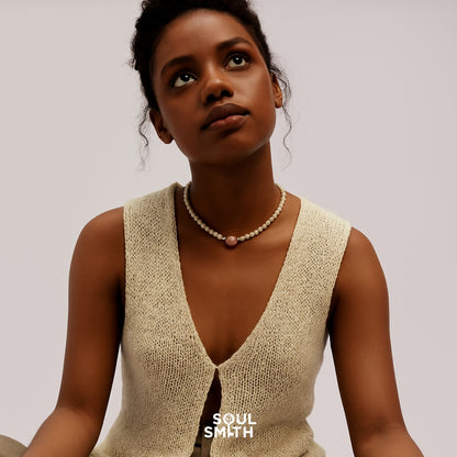 Woman wearing a delicate Soulsmith necklace featuring a central Pink Morganite charm and creamy ivory beads, styled with a natural knit sleeveless top, evoking softness and serenity.
