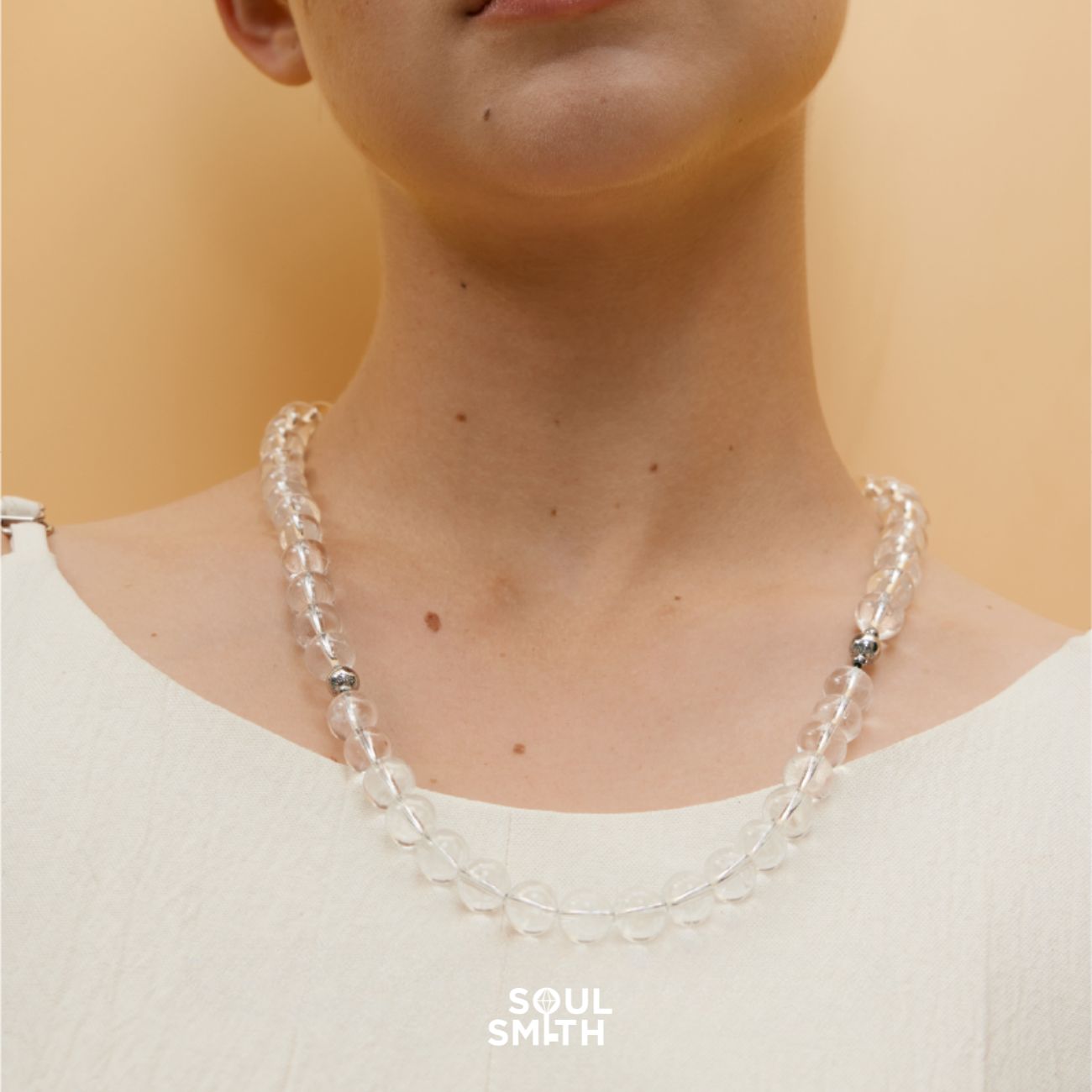 Model wearing a Soulsmith Clear Quartz necklace featuring smooth, round crystal beads and magnetic clasp, styled over a light neutral-toned top for a minimalist, spiritual aesthetic.
