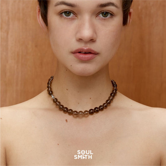 Smoky Quartz crystal necklace with polished dark translucent beads, elegantly styled on model’s neck against a warm wooden background