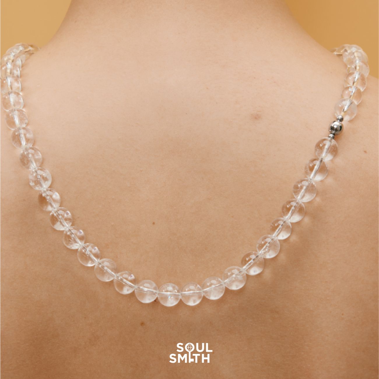 Close-up of Soulsmith Clear Quartz necklace draped across the back, showcasing polished round crystal beads and a magnetic clasp for energy alignment and minimalist elegance.
