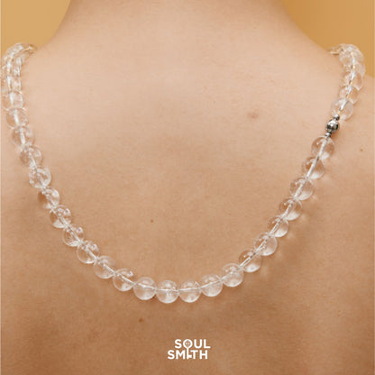 Close-up of Soulsmith Clear Quartz necklace draped across the back, showcasing polished round crystal beads and a magnetic clasp for energy alignment and minimalist elegance.
